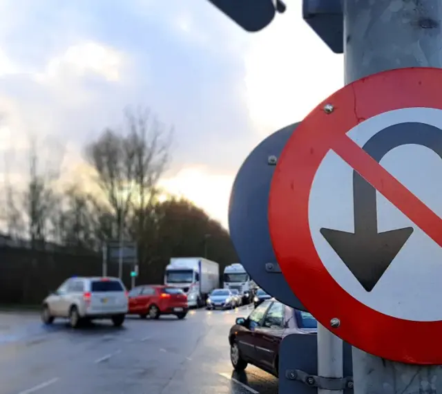 Znak zakazu zawracania na skrzyżowaniu. Samochody stoją w deszczu, czekając na zielone światło.