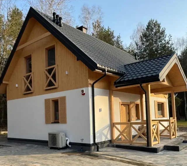 Nowy dom w lesie, drewniane elementy i biały tynk. Prowadzenie budowy domu zakończone sukcesem, gotowy do zamieszkania.