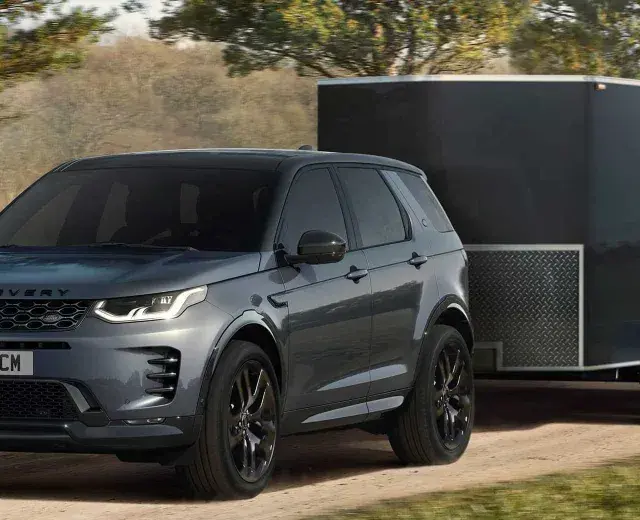 Szary Land Rover Discovery Sport z przyczepą o masie 2000 kg jedzie po leśnej drodze.