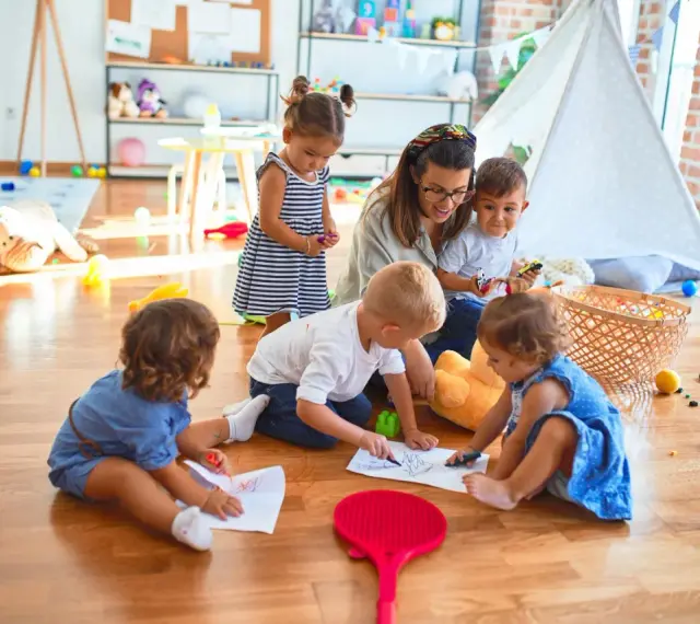 Niania w Warszawie, opiekująca się grupą dzieci, które rysują na podłodze. Zastanawiasz się, ile zarabia niania w Warszawie?