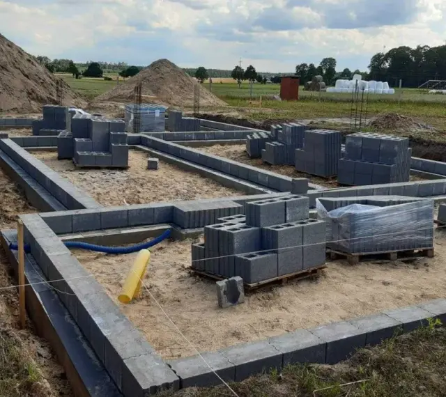 Budowa fundamentów z bloczków betonowych. Zastanawiasz się, ile kosztuje wylanie fundamentu? Na placu budowy widać materiały i postęp prac.