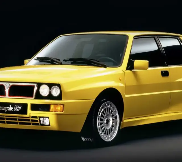 Żółta Lancia Delta Integrale HF z lat 90. na czarnym tle, z charakterystycznym grillem i felgami.