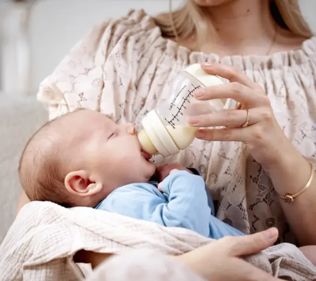 Mama karmi maluszka z butelki, która może być najlepszą butelką antykolkową dla noworodka.