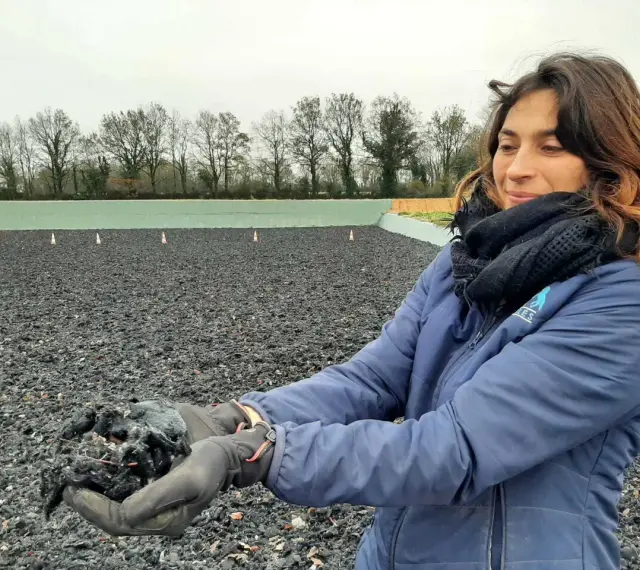 Une femme tient dans ses mains un échantillon de fibre, un avis carrière en fibre. L'arrière-plan montre une carrière équestre.