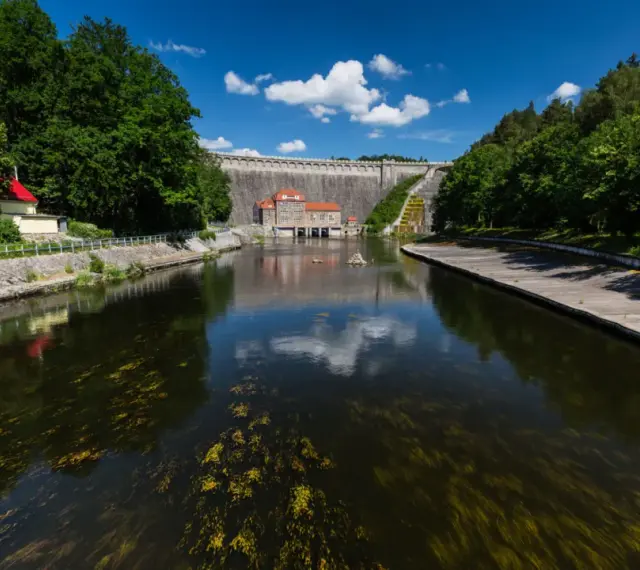 Zapora Pilchowice trasa. Malownicza droga nad zbiornikiem wodnym, z widokiem na monumentalną budowlę i otaczającą zieleń.