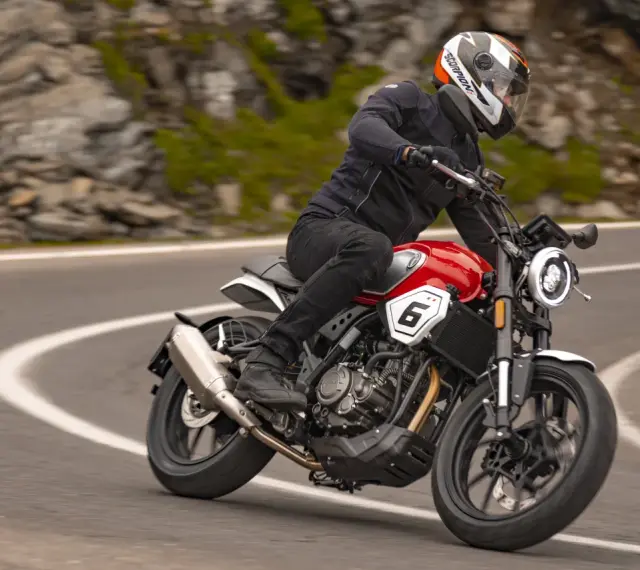Motocyklista w kasku jedzie czerwonym motocyklem po krętej drodze. Idealny motocykl na początek przygody z jazdą.