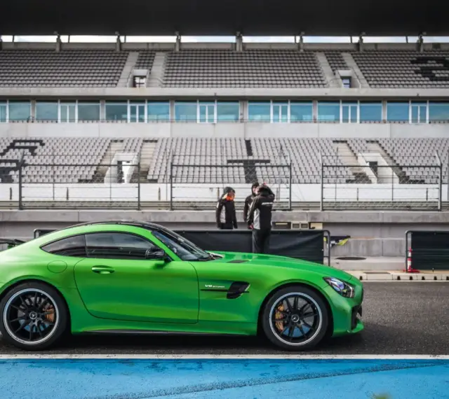 Zielony Mercedes GTR na torze wyścigowym, gotowy do jazdy. Za nim puste trybuny stadionu.