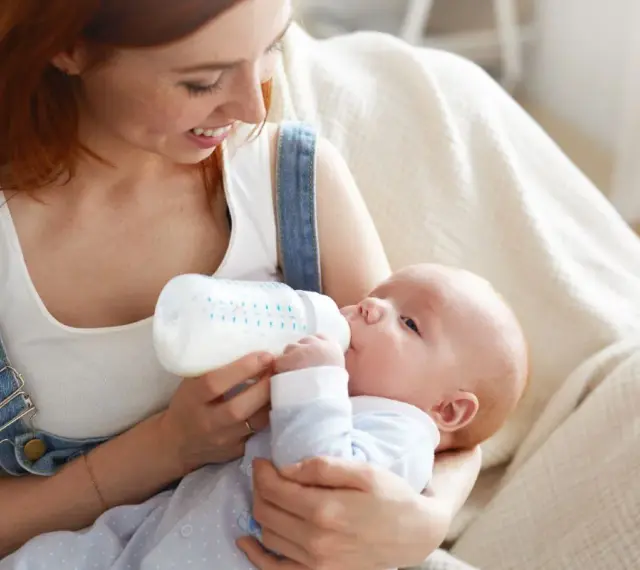 Uśmiechnięta mama karmi piersią swoje dziecko z butelki, szukając najlepszych butelek dla noworodka.