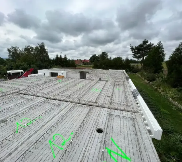 Gotowy do wylania strop, zbrojenie czeka na beton. W tle drzewa i pochmurne niebo.