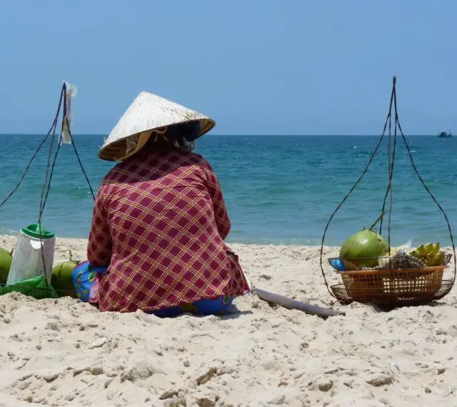 Sprzedawczyni kokosów na plaży w Mui Ne, Wietnam. W tle błękitne morze i niebo.