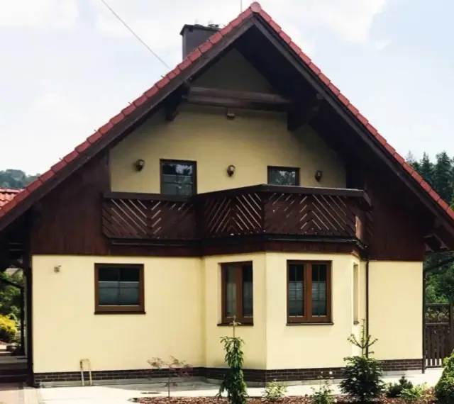 Jasny dom z drewnianymi elementami i balkonem, otoczony zielenią. Może to być dom Adama Małysza w Wiśle.