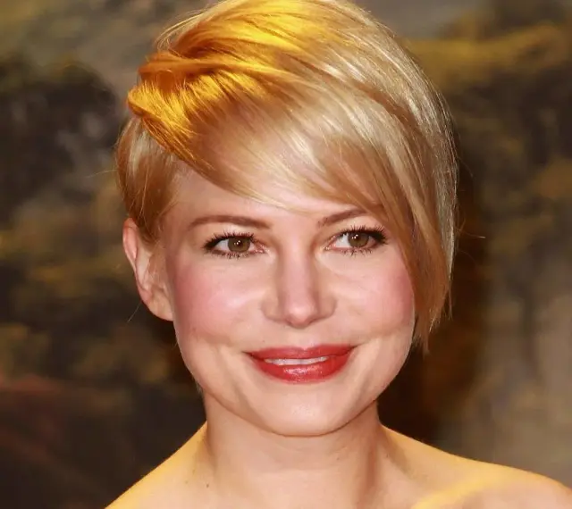 Uśmiechnięta kobieta z okrągłą twarzą i blond fryzurą, z burzą złotych włosów opadających na czoło.