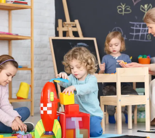Opiekunka dziecięca z dziećmi buduje rakietę z klocków.