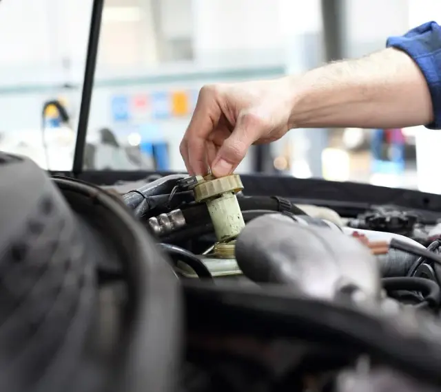 Ręka mechanika dokręca korek zbiorniczka płynu hamulcowego. Czas na badanie techniczne po terminie, by uniknąć problemów.