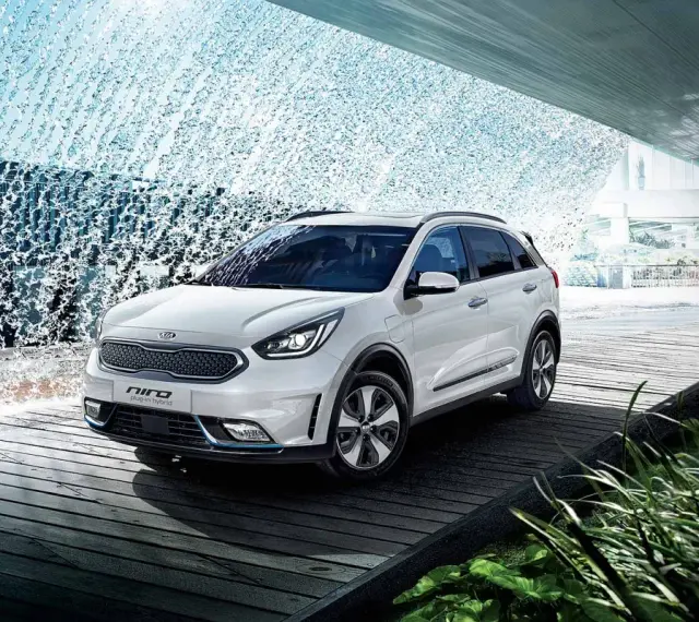 Biały Kia Niro Plug-in Hybrid na drewnianej platformie, otoczony wodnymi kaskadami i zielenią.