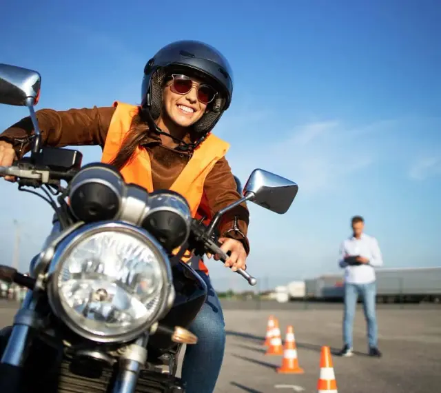 Uśmiechnięta kursantka na motorze, w kasku i kamizelce, uczy się jeździć. Zastanawiasz się, ile kosztuje prawo jazdy na motor?