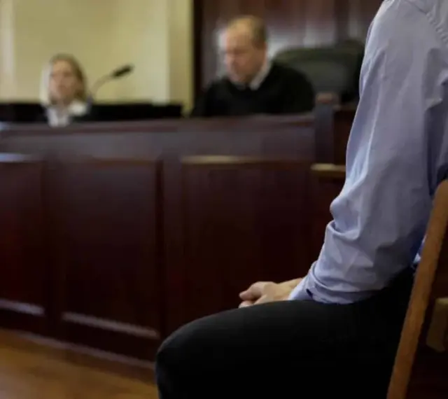 Osoba siedzi w ławie sądowej, czekając na decyzję w sprawie zgodnej z art. 37a. Sąd obraduje.