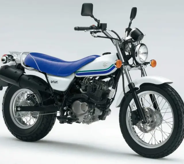 Biały Suzuki Van Van 125 z niebieskim siedzeniem i zielono-niebieskimi paskami na baku. Idealny na miejskie przygody.