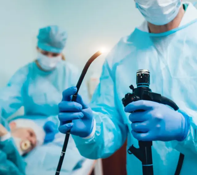 Lekarz w niebieskich rękawiczkach trzyma endoskop podczas gastroskopii.