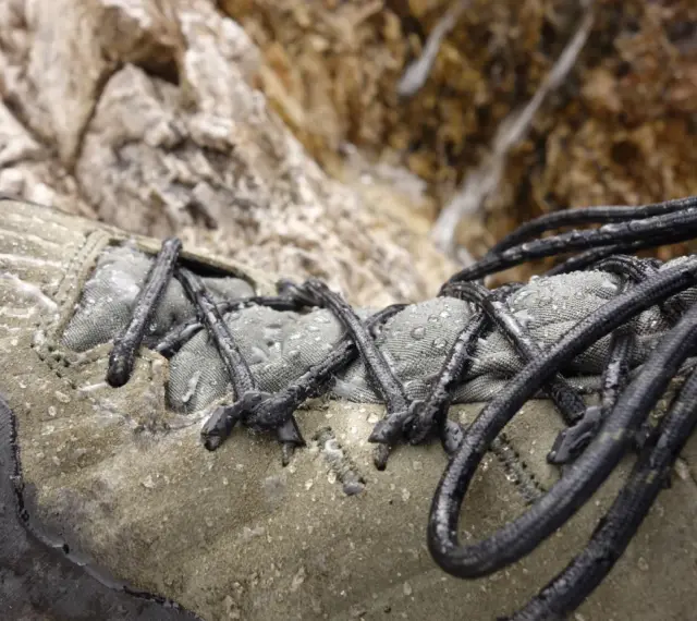 Zbliżenie na mokry, zielony but trekkingowy z czarnymi sznurówkami na tle kamieni.