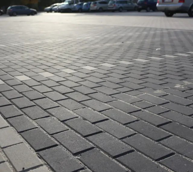 Szary parking wyłożony kostką brukową holland. W tle widać zaparkowane samochody.