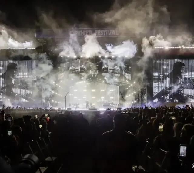 Koncert Linkin Park na Opener Festival. Tłum ludzi z telefonami, dym i światła na scenie.