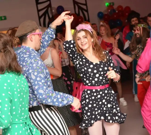 Impreza w stylu PRL! Kobieta w grochy i mężczyzna w paski tańczą. Idealny strój na imprezę w stylu PRL to kolorowe wzory i dodatki.