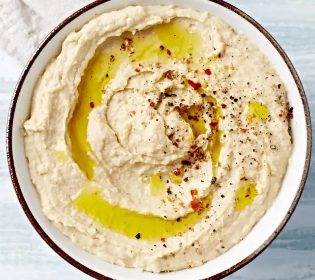 Kremowy, gładki hummus polany oliwą i posypany przyprawami. Idealny do maczania pieczywa.