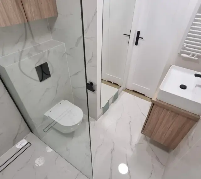 Nowoczesna łazienka z prysznicem walk-in, umywalką nablatową i podwieszaną toaletą. Eleganckie płytki imitujące marmur i drewniane akcenty. Remont łazienki koszt może być różny, ale efekt jest wart inwestycji.