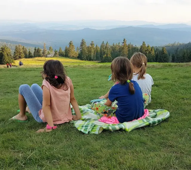 Trzy dziewczynki siedzą na trawie, podziwiając widok z rysianka wysokość.