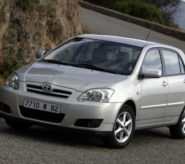 Srebrna Toyota Corolla E12 na krętej drodze, z kamienistym zboczem w tle.