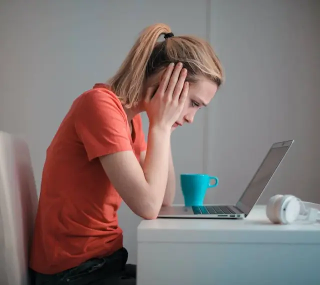 Zmartwiona kobieta przy laptopie, zastanawia się, czy porzucenie pracy wlicza się do emerytury. Na biurku kubek i słuchawki.