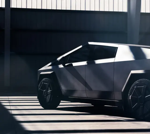 Tesla Cybertruck w ciemnym wnętrzu, widok z boku, podkreślony przez światło i cień.
