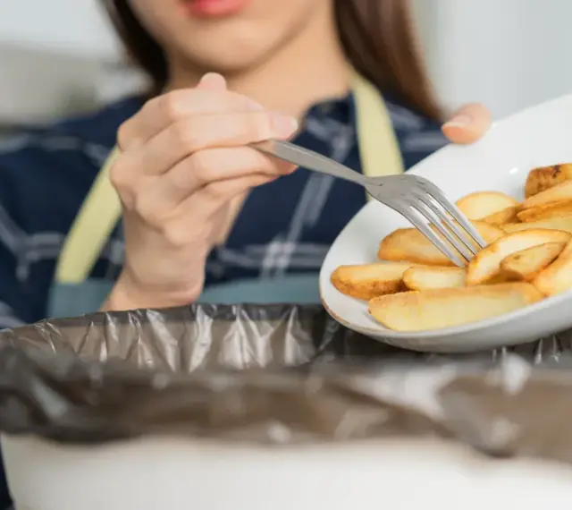 Kobieta wyrzuca frytki, zaczynając drogę do tego, jak obniżyć cholesterol bez leków. Zdrowa dieta to klucz.