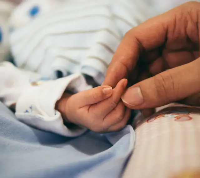 Dłoń rodzica obejmuje maleńką dłoń dziecka. To symbol miłości i troski, a także przygotowań do złożenia wniosku o urlop macierzyński.
