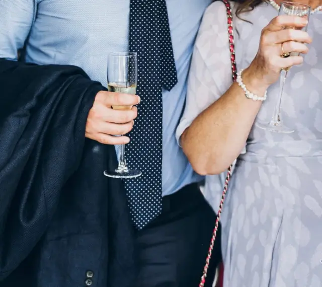 Elegancki mężczyzna w garniturze i krawacie, trzymający kieliszek szampana. To idealny strój, co się ubiera na bierzmowanie.