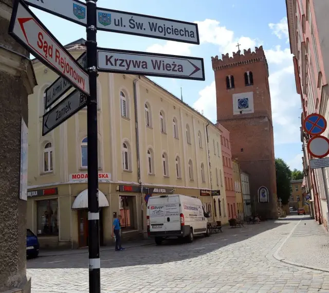 Ulica z wieżą i drogowskazami do Sądu Rejonowego, Krzywej Wieży i Zamku. Odkryj mało znane miejsca na Dolnym Śląsku.