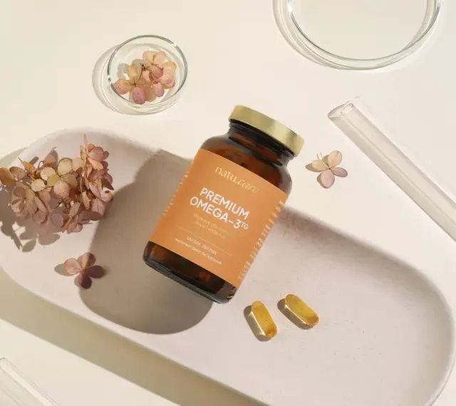 Suplement Omega-3 z DHA dla kobiet w ciąży, wspierający rozwój mózgu dziecka. Delikatne kapsułki na białej tacy z suszonymi kwiatami.