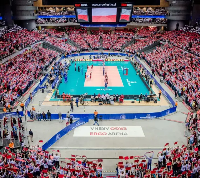 Widownia Ergo Areny, wypełniona kibicami z flagami Polski, dopingująca mecz siatkówki. Ogromna pojemność hali robi wrażenie.