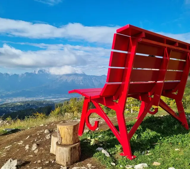 La panchina gigante sul Nevegal, rossa e imponente, domina un panorama mozzafiato di montagne e vallate sotto un cielo azzurro.
