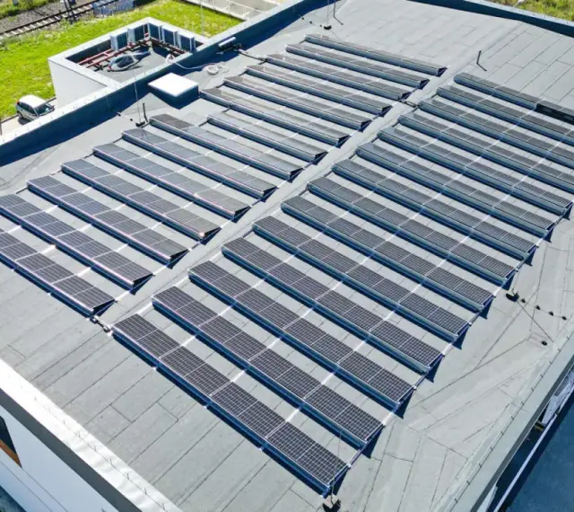 Duży dach płaski pokryty panelami fotowoltaicznymi, które zbierają energię słoneczną.