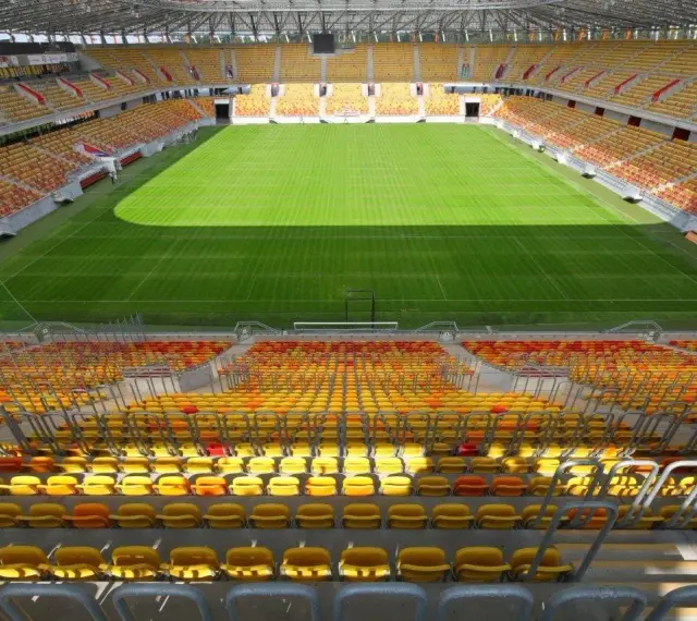 Pusta trybuna stadionu Jagiellonii, z żółtymi i czerwonymi siedzeniami. Pojemność obiektu robi wrażenie.