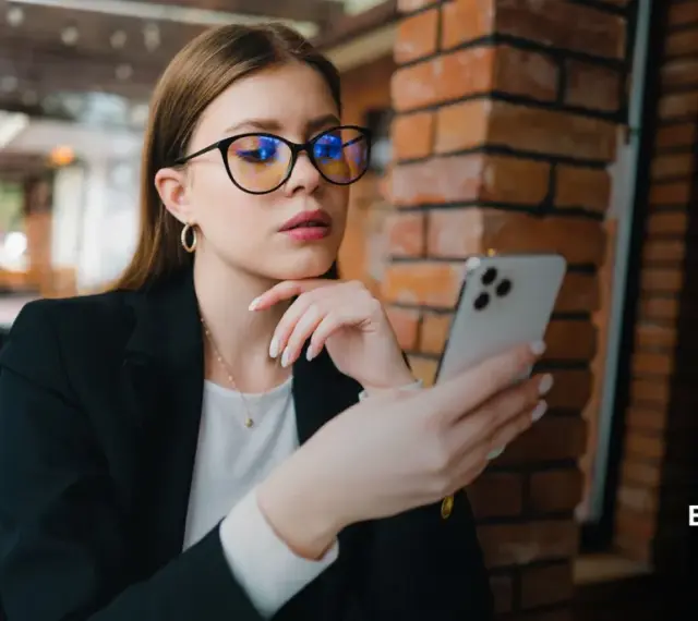 Kobieta w okularach z niebieskimi filtrami przegląda telefon. Różne rodzaje okularów mogą chronić wzrok.