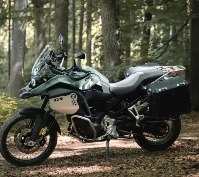 Zielony motocykl BMW F900GS z kuframi, gotowy na przygodę w lesie.