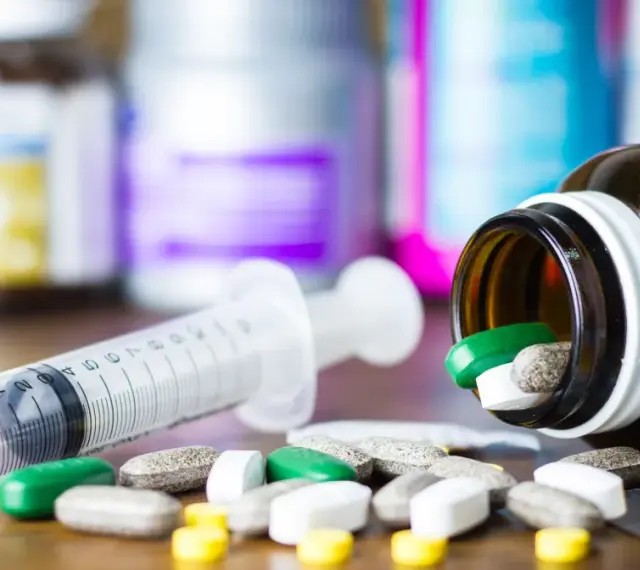 Leki, w tym zielone tabletki, rozsypane obok strzykawki i buteleczki. Może to być methocarbamol.