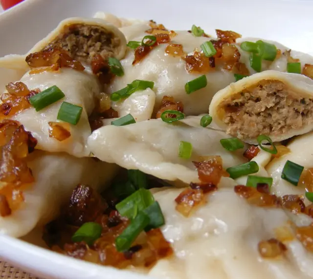 Domowe pierogi z mięsem, posypane smażoną cebulką i szczypiorkiem.