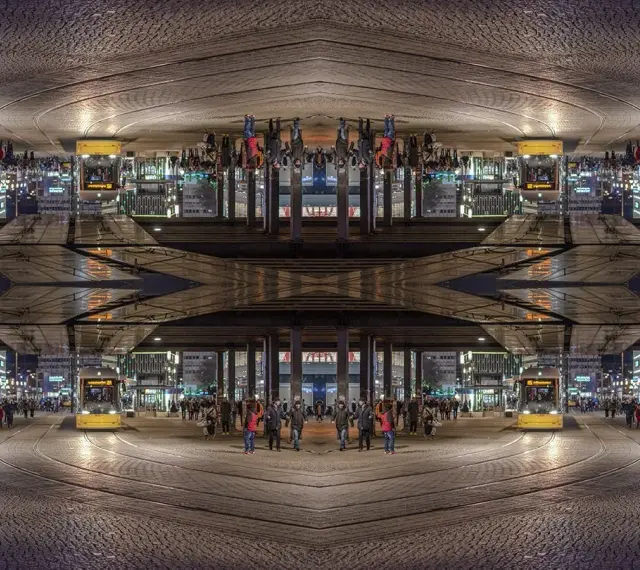 Nocne miasto z żółtym tramwajem i ludźmi. Kompozycja symetryczna tworzy surrealistyczny, odbity świat.