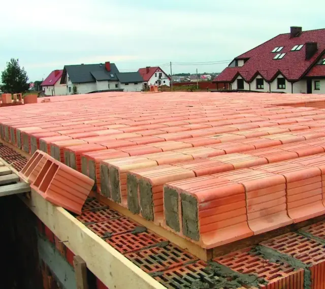 Budowa stropu ackermana z pustaków ceramicznych. W tle domy jednorodzinne.