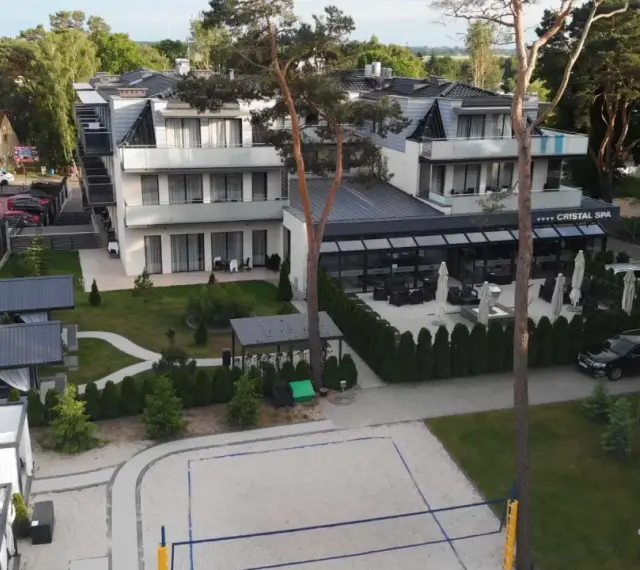 Nowoczesny hotel Cristal Spa z basenem i kortem do siatkówki plażowej, otoczony zielenią.