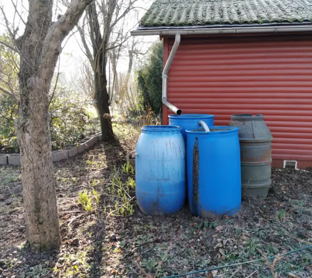 Zbiorniki na deszczówkę przy czerwonym budynku. Prawda o rzekomym opodatkowaniu deszczówki zbieranej na prywatnych posesjach jest taka, że nie ma takiego podatku.
